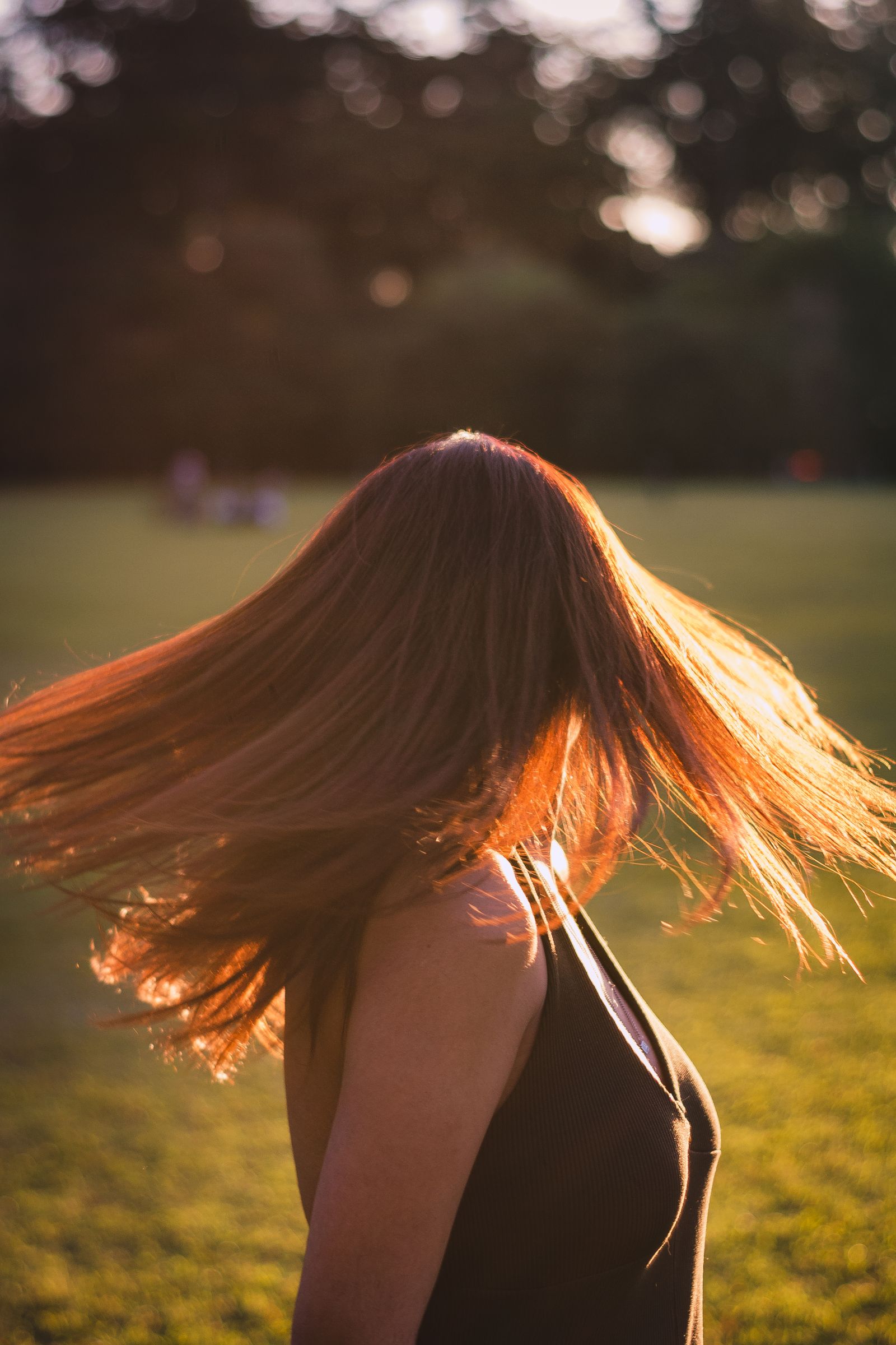 Adult woman with flowing brunette hair in a sunlit park setting. Vibrant and dynamic portrait outdoors.