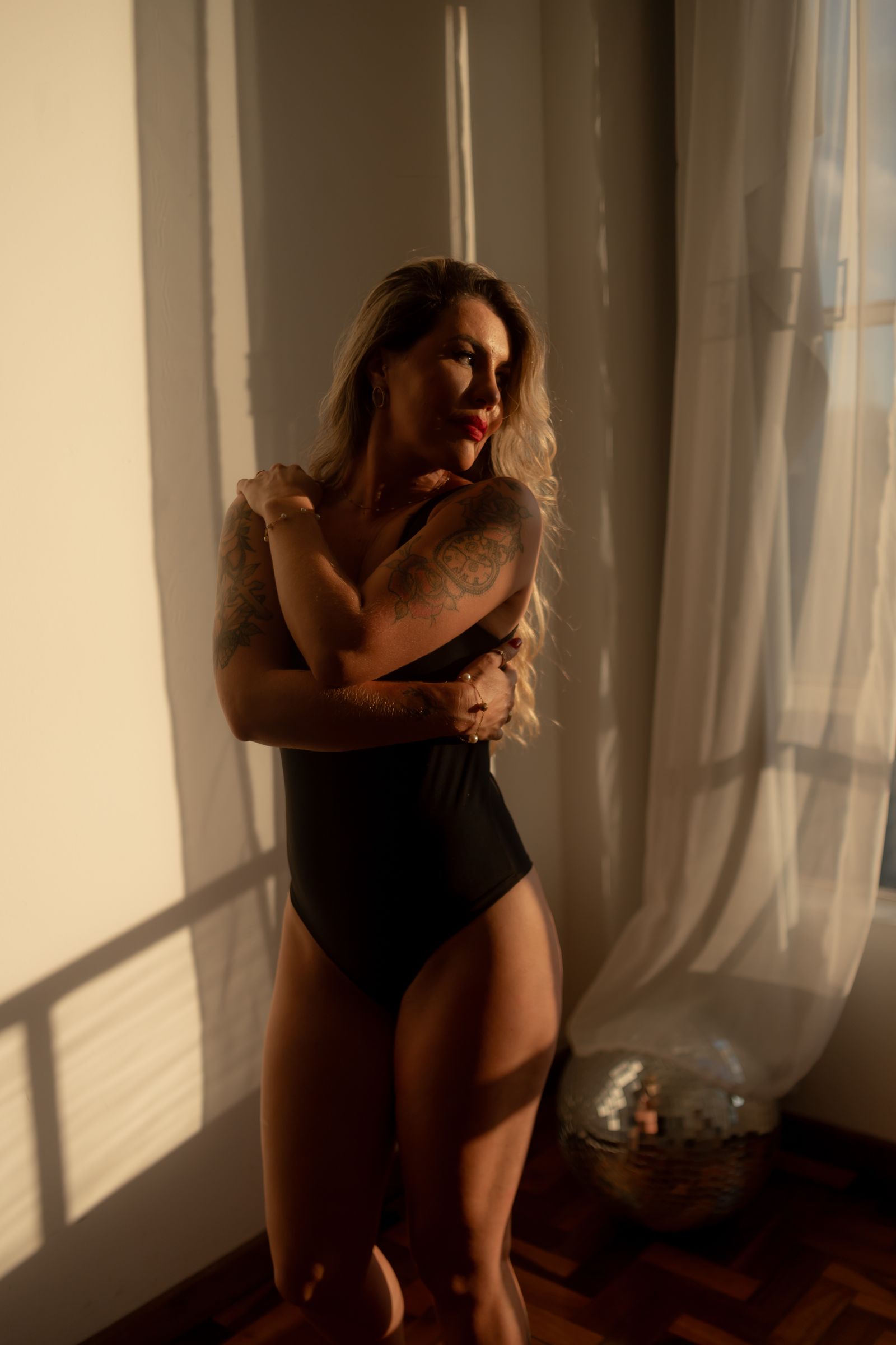 A woman embraces herself in soft sunlight, showcasing self-love and grace.